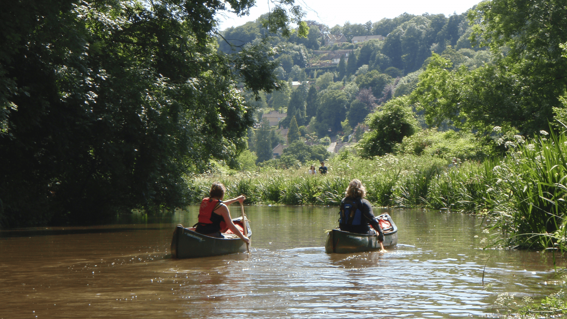 Two women paddling canoes down a quiet river.