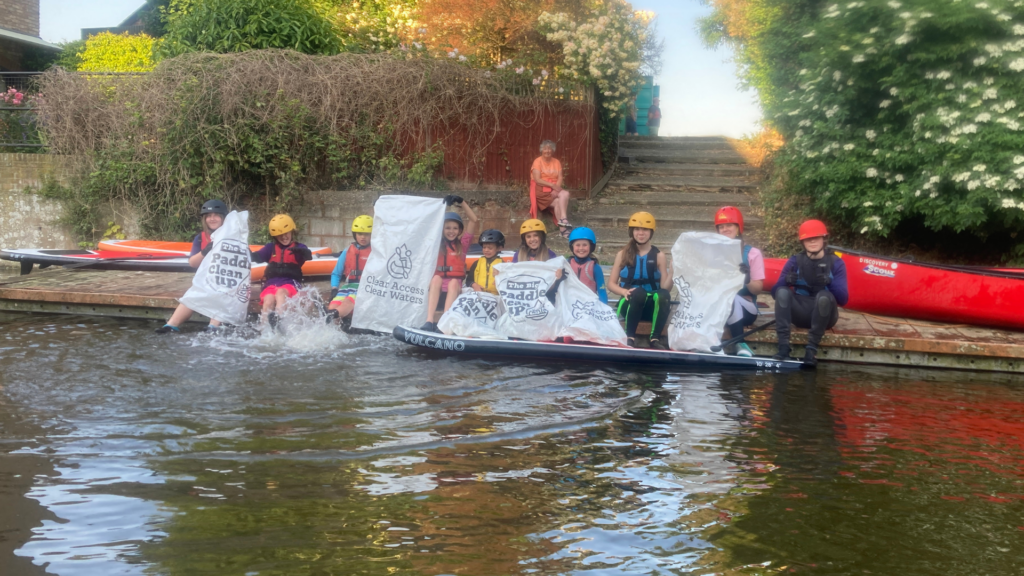 Kids with feet in the water on a riverbank after taking part in a Big Paddle Cleanup.