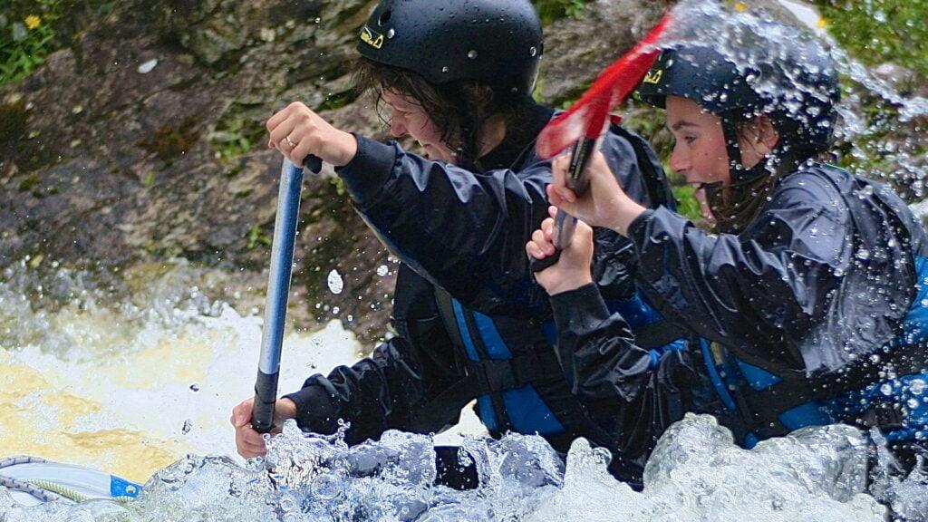Two women paddling in lively white water.