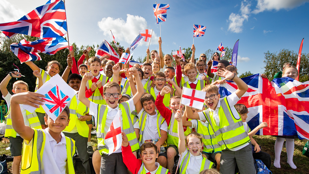 Spectators at an event. Children holding union flags in a crowd cheering on athletes.