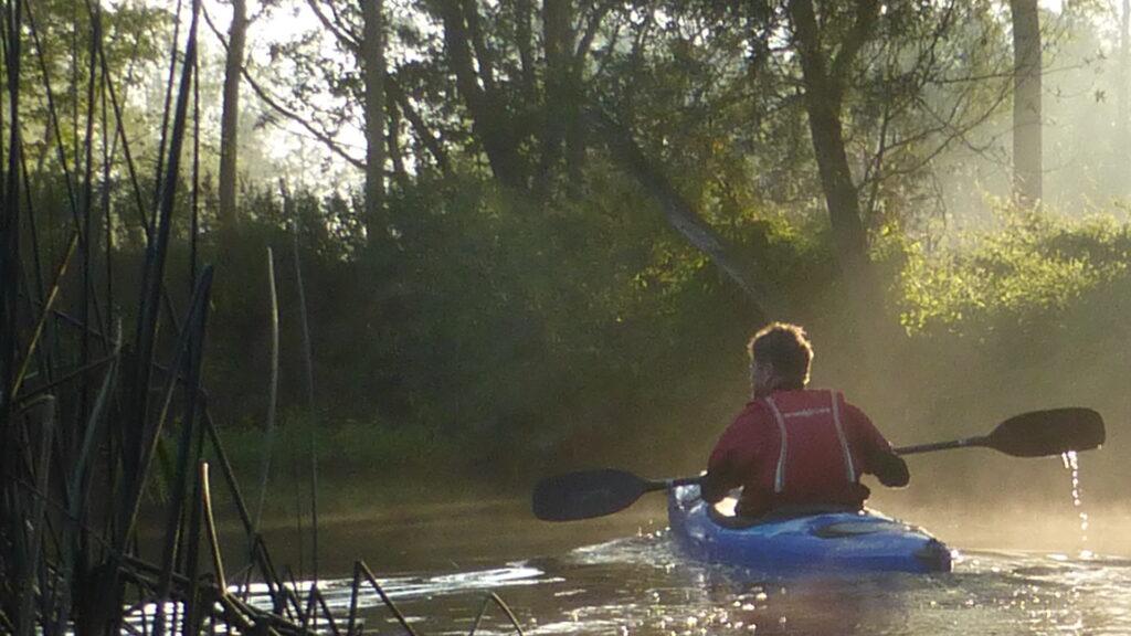 Paddler in kayak on misty morning with sunlight right of image