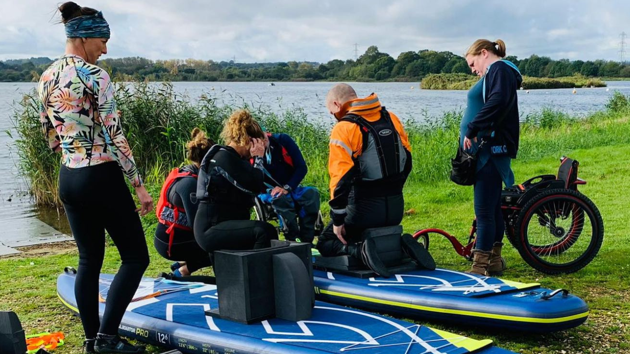 Paddlers taking part in a Ripple Rebels paddleboard day, two with wheelchairs.