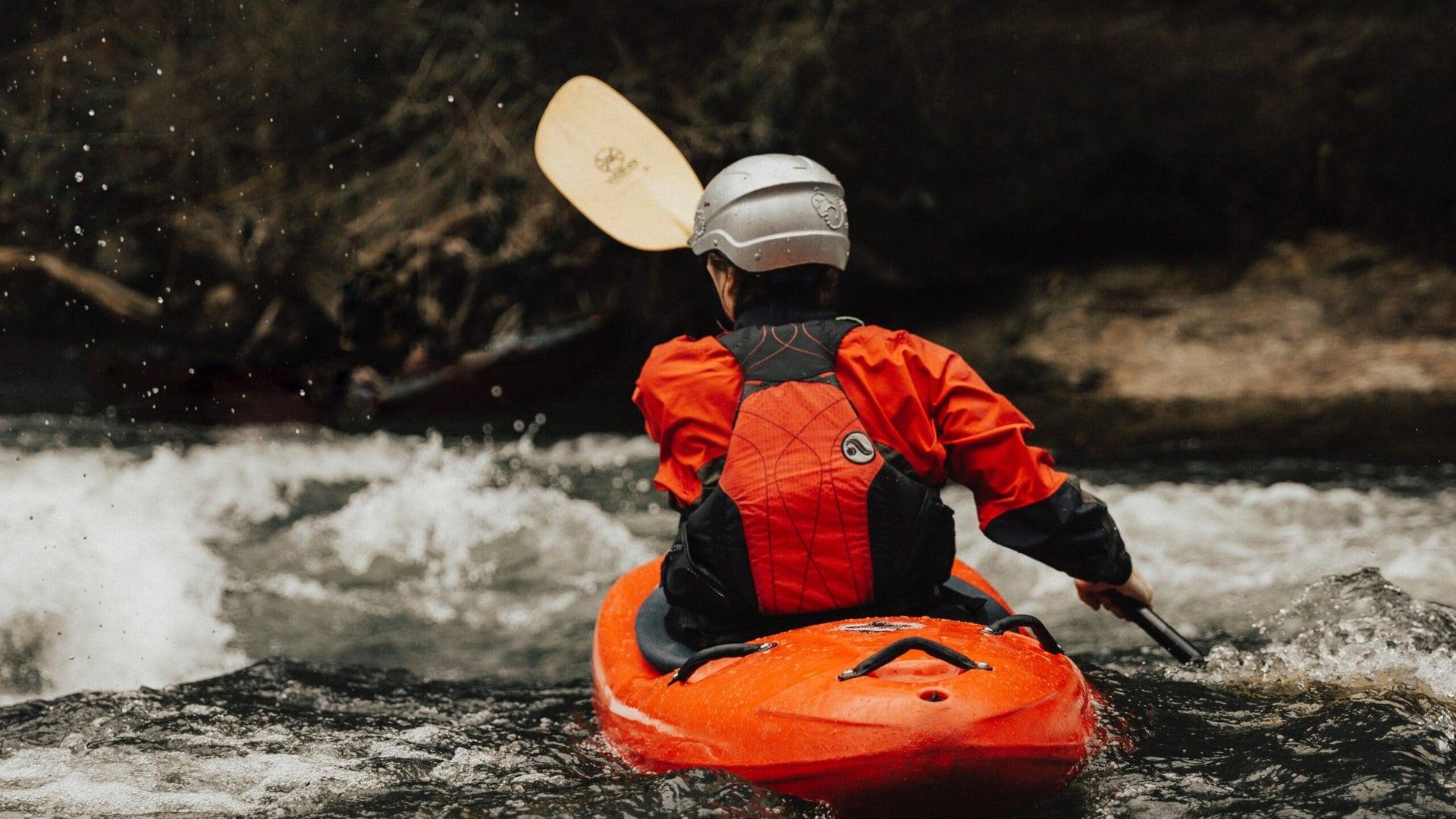 Woman in orange kayak paddling in white water