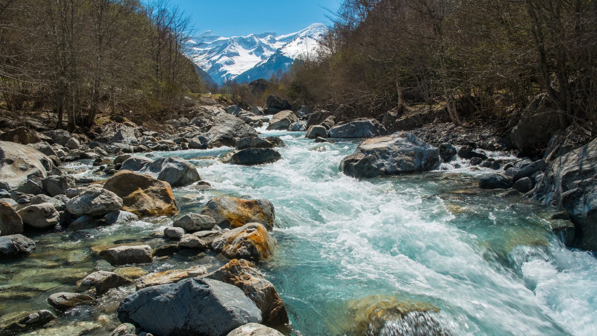 Image of a river flowing with the snow capped mountains in the background.