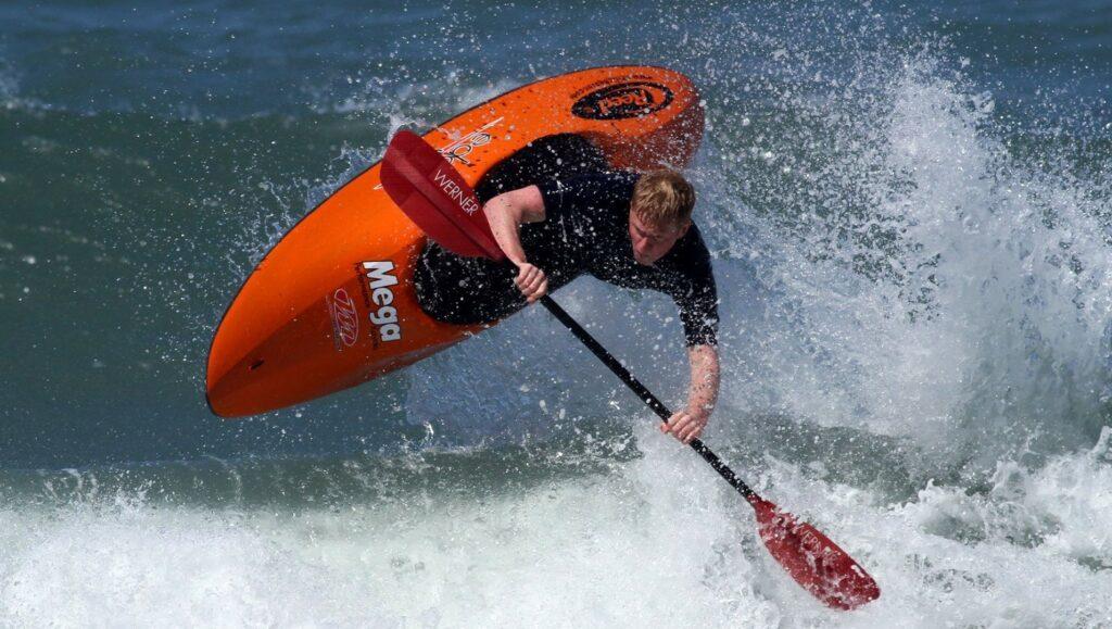 Surf kayaker in action on the sea in orange kayak.