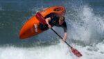 Surf kayaker in action on the sea in orange kayak.