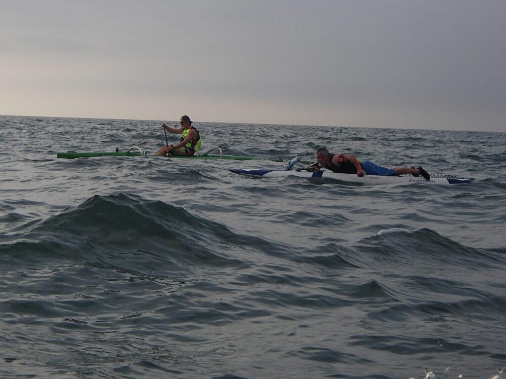 Dean lying on his paddleboard and Niall in canoe paddling at Sea