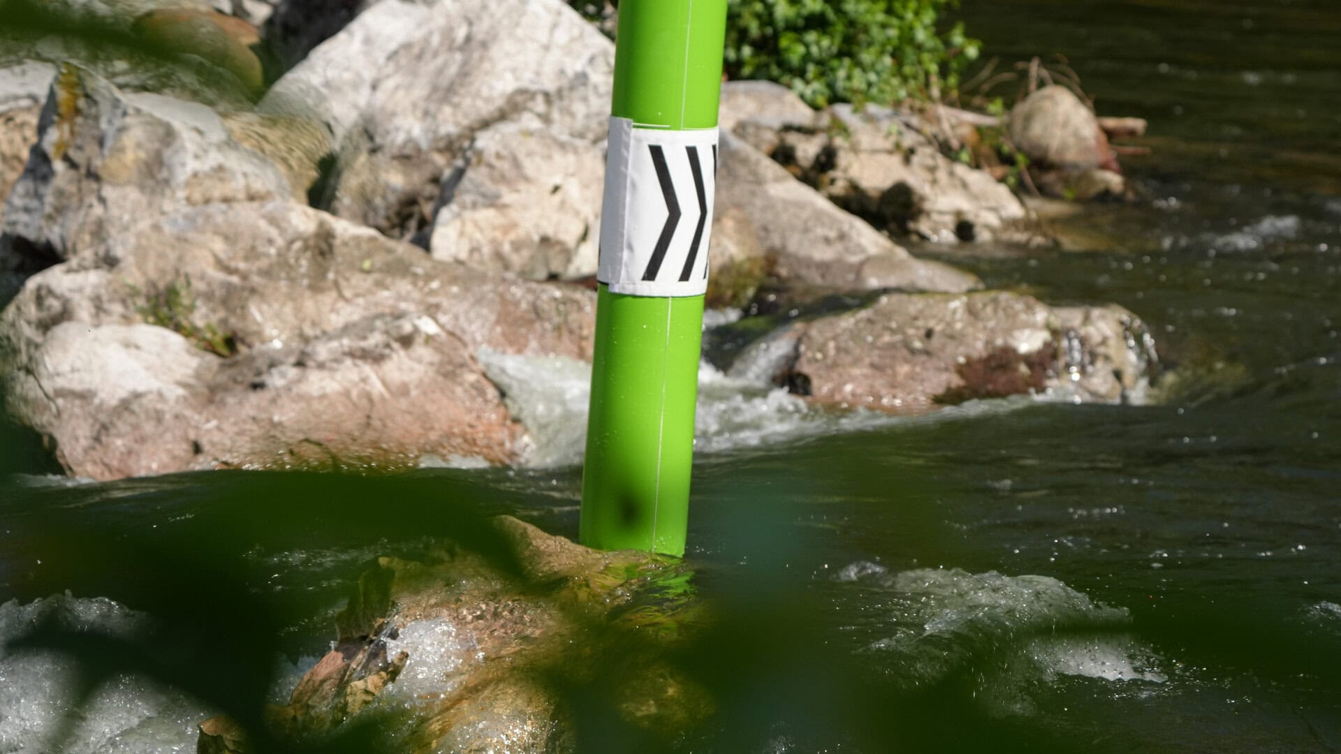 Kayak cross green inflatable pole hanging over whitewater.