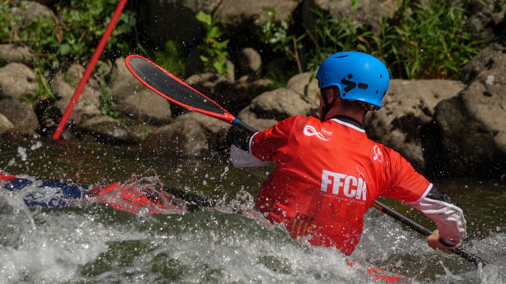U23 athlete paddler hard through whitewater in kayak cross.