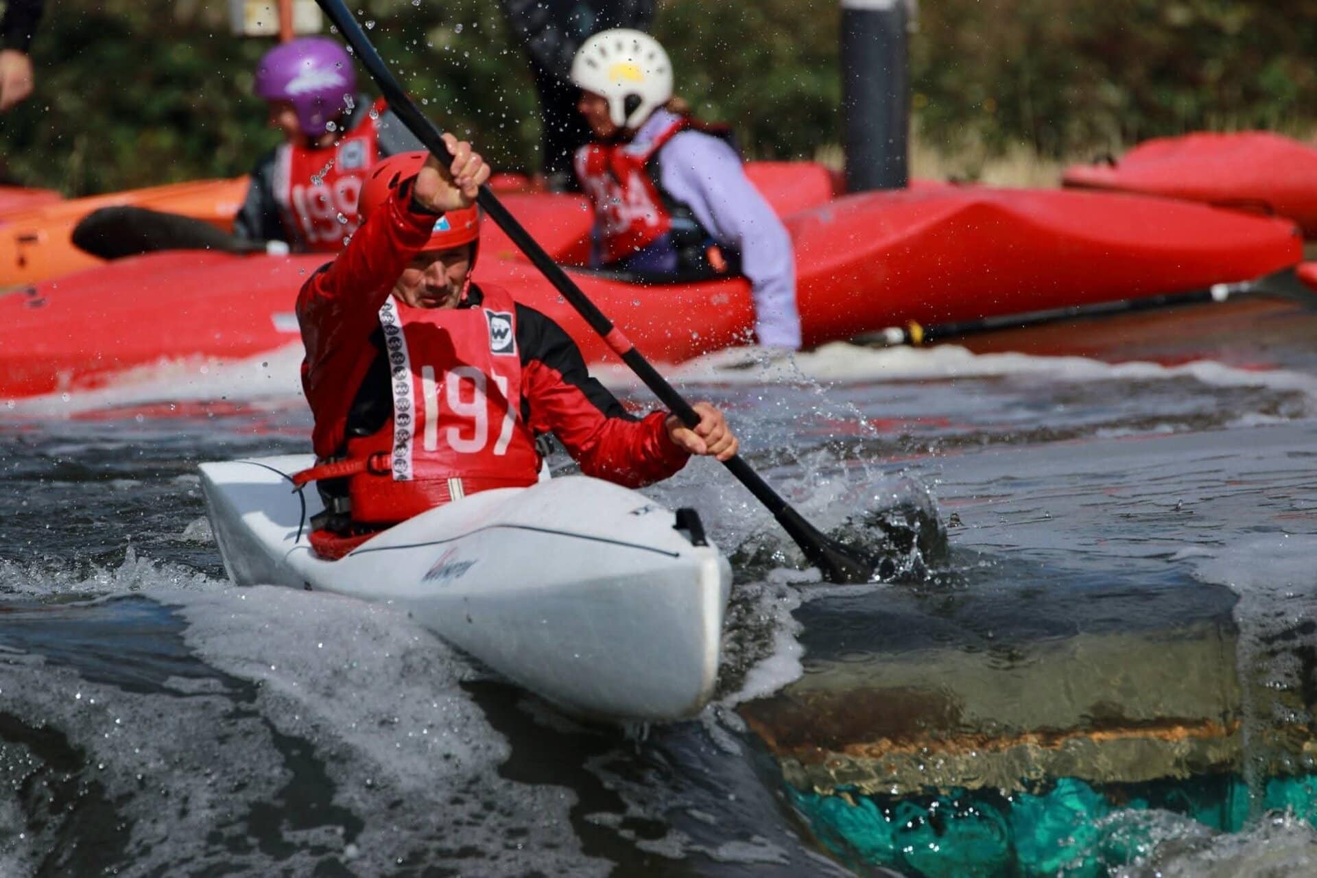 A paddler in a red bib paddling over whitewater.
