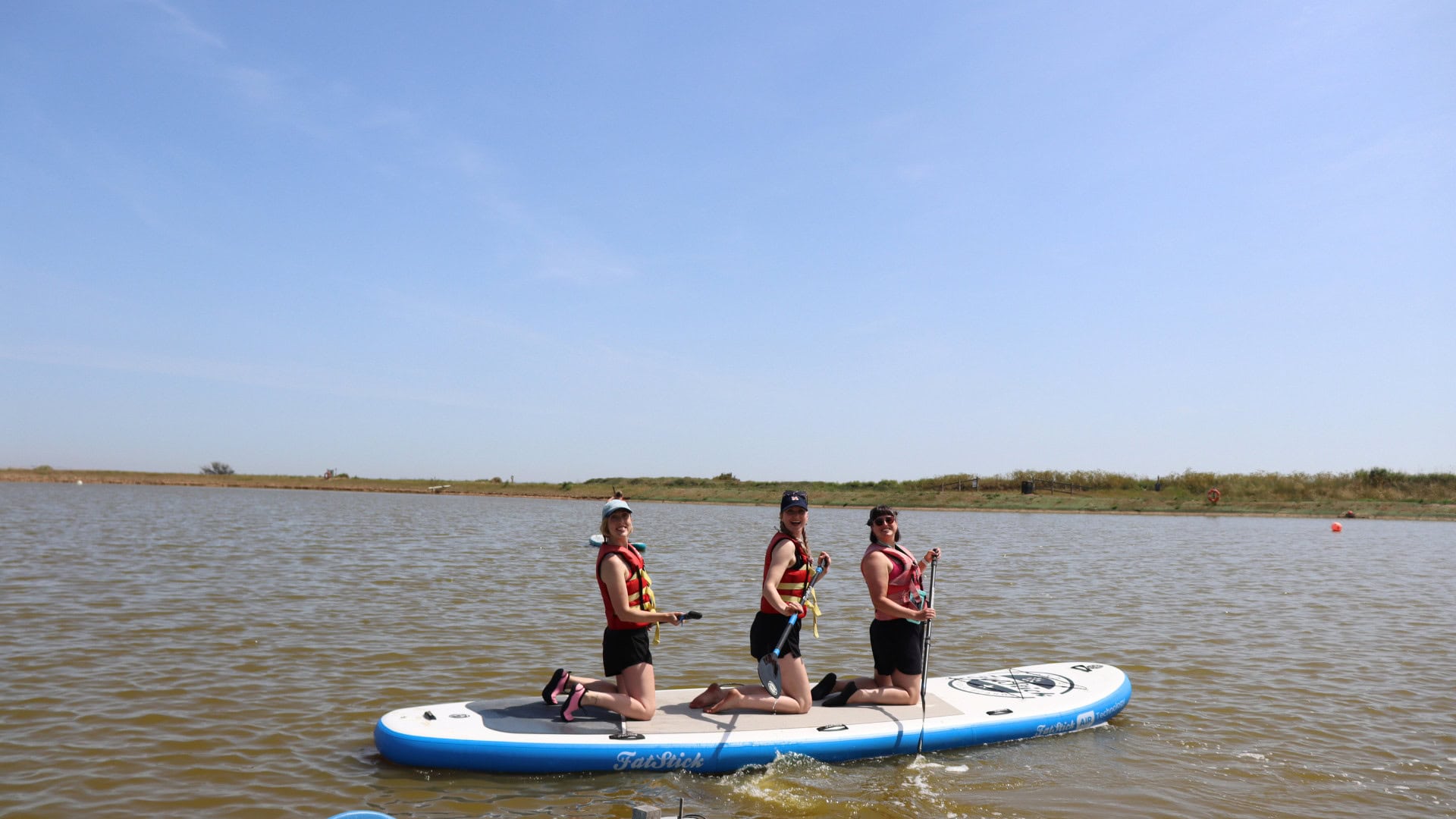 Group of three females on a large stand up paddleboard at Mersea Water Park for the #ShePaddlesWeekender 2025